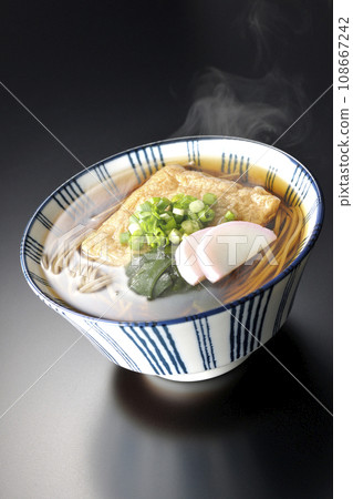 黑色背景下拍攝的熱狐蕎麥麵,配上炸豆腐、魚糕、裙帶菜和蔥 黑色背景下拍攝的熱狐蕎麥麵,配上炸豆腐、魚糕、裙帶菜和蔥 108667242