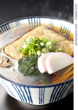 Hot fox soba with fried tofu, kamaboko, wakame, and green onion photographed against a black background Hot fox soba with fried tofu, kamaboko, wakame, and green onion photographed against a black background 108667247