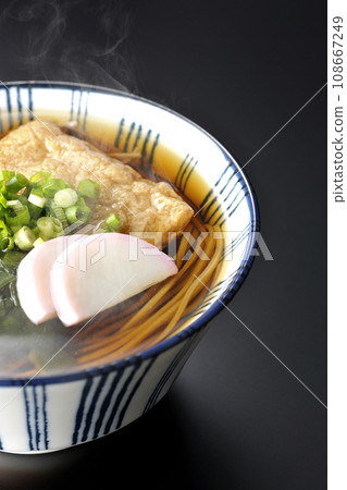 黑色背景下拍攝的熱狐蕎麥麵,配上炸豆腐、魚糕、裙帶菜和蔥 黑色背景下拍攝的熱狐蕎麥麵,配上炸豆腐、魚糕、裙帶菜和蔥 108667249