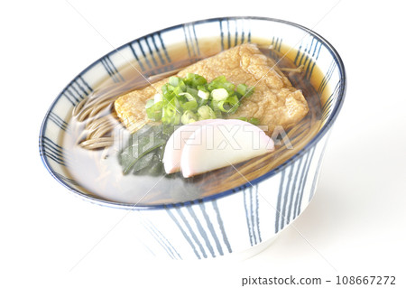 Hot fox soba topped with fried tofu, kamaboko, wakame, and green onions, photographed against a white background Hot fox soba topped with fried tofu, kamaboko, wakame, and green onions, photographed against a white background 108667272