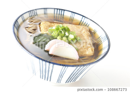 Hot fox soba topped with fried tofu, kamaboko, wakame, and green onions, photographed against a white background 108667273
