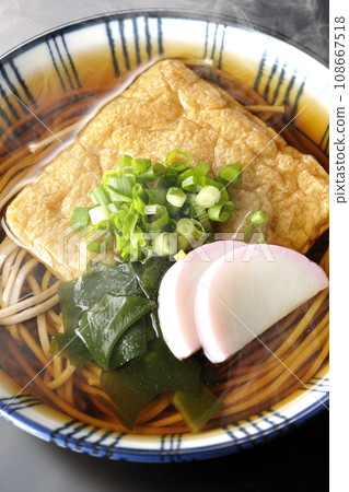 黑色背景下，頭頂上放著熱騰騰的狐狸蕎麥麵，上面放著炸豆腐、魚板、裙帶菜和蔥 108667518