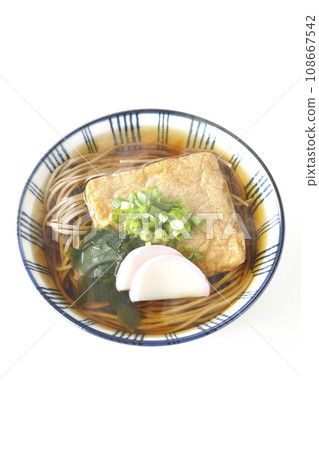 白色背景下，頭頂上放著熱騰騰的蕎麥麵，上面放著炸豆腐、魚板、裙帶菜和蔥 108667542