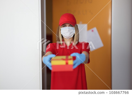 Woman courier in protective medical mask and gloves giving gift Woman courier in protective medical mask and gloves giving gift 108667766