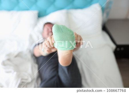 Man lying on bed and putting on green sock closeup 108667768