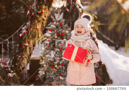 Little girl with a Christmas gift outdoors in winter on Christmas Eve. Little girl with a Christmas gift outdoors in winter on Christmas Eve. 108667769