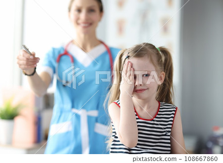 Little girl covering her eyes with her hand at ophthalmologist appointment Little girl covering her eyes with her hand at ophthalmologist appointment 108667860