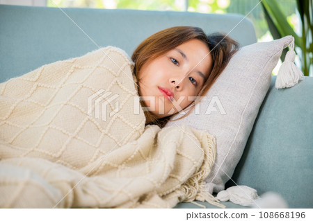 Sick female cold high fever covered with blanket resting sleeping at home, Asian young woman have problem with headache lying on sofa in living room, Unhappy sick girl, medicine 108668196