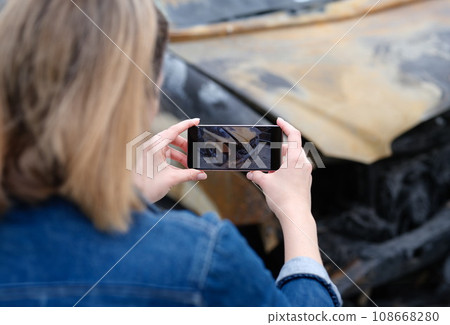 insurance agent or investigator takes picture on smartphone of car after arson insurance agent or investigator takes picture on smartphone of car after arson 108668280