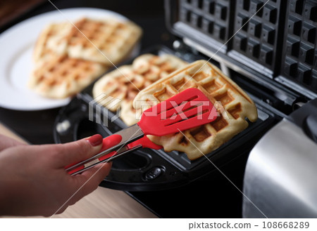 Female hands finishing making waffles on waffle iron in bakery Female hands finishing making waffles on waffle iron in bakery 108668289