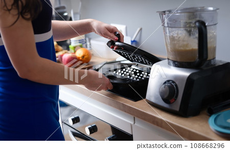 Woman opens electric waffle maker for Viennese and Belgian waffles. Woman opens electric waffle maker for Viennese and Belgian waffles. 108668296