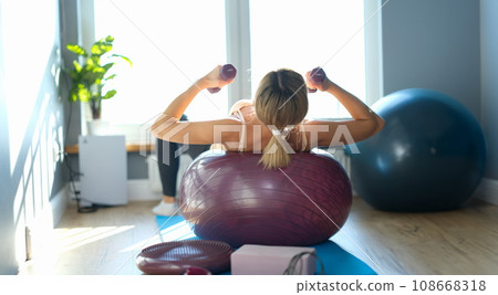 Woman is engaged in fitball and holds dumbbells 108668318