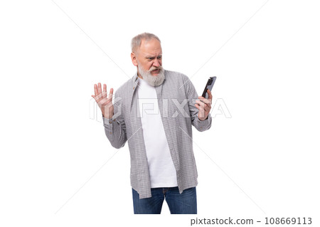 handsome gray-haired elderly man in a shirt is trying to figure out the phone on a white background handsome gray-haired elderly man in a shirt is trying to figure out the phone on a white background 108669113