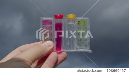 Water samples for PH and chlorine levels. Hand holding against the sky - checking the quality of water in the pool Water samples for PH and chlorine levels. Hand holding against the sky - checking the quality of water in the pool 108669437
