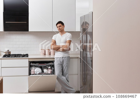 handsome guy using dishwasher and washing dishes in white modern kitchen. copy space 108669467