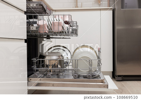 Open built-in dishwasher machine with clean cutlery, dishes, plates in white modern kitchen. side view 108669510