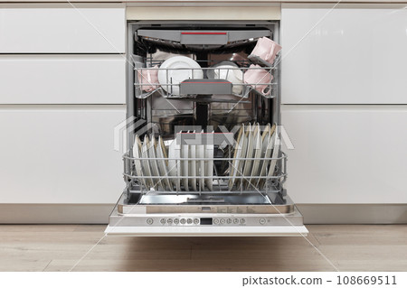 Open built-in dishwasher machine with clean cutlery, dishes, plates in white modern kitchen. front view 108669511