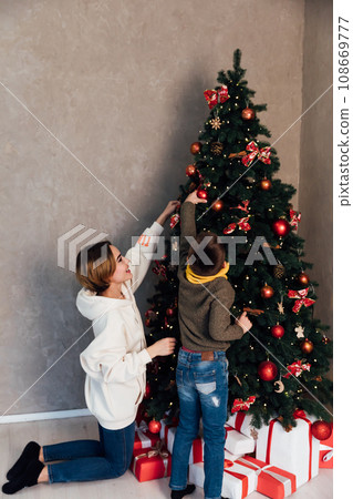mother and son decorate the Christmas tree for the holiday New Year Christmas mother and son decorate the Christmas tree for the holiday New Year Christmas 108669777