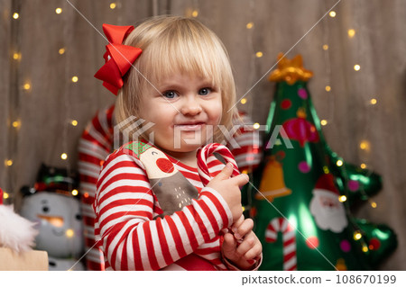 Little two-year-old girl eating lollipop at Christmas while sitting at home among gifts Little two-year-old girl eating lollipop at Christmas while sitting at home among gifts 108670199