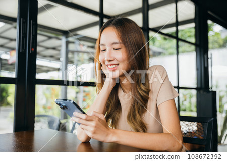 Asian young woman using smart phone for shopping online at cafe coffee shop in the morning, female has transfer money financial internet banking on mobile phone 108672392