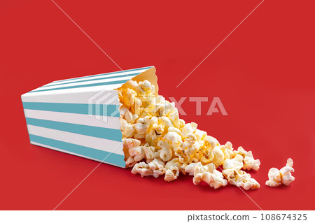 Tasty cheese popcorn falling out of a turquoise striped carton bucket, isolated on red background 108674325