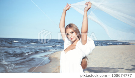 Happy blonde woman is catching clouds and wind with her arms on the ocean beach 108674777