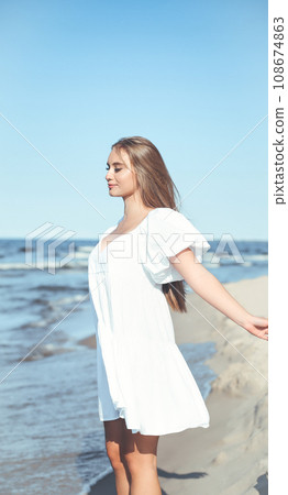 Happy, beautiful woman on the ocean beach standing in a white summer dress, open arms Happy, beautiful woman on the ocean beach standing in a white summer dress, open arms 108674863
