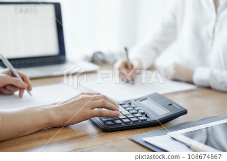 Two accountants using a laptop computer and calculator while counting taxes at wooden desk in office. Teamwork in business audit and finance 108674867