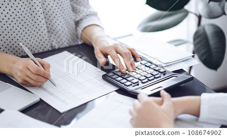 Woman accountant using a calculator and laptop computer while counting taxes with a client or a colleague. Business audit team, finance advisor 108674902