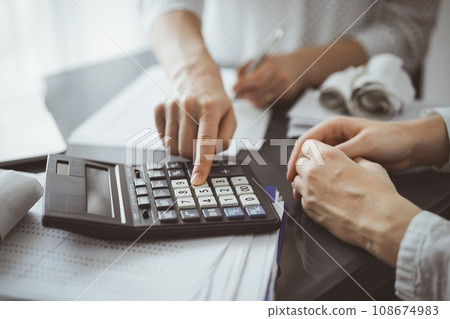 Woman accountant using a calculator and laptop computer while counting taxes for a client. Business audit and finance concepts 108674983