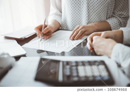 Woman accountant using a calculator and laptop computer while counting taxes for a client. Business audit and finance concepts Woman accountant using a calculator and laptop computer while counting taxes for a client. Business audit and finance concepts 108674988