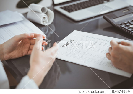 Woman accountant using a calculator and laptop computer while counting taxes for a client. Business audit and finance concepts Woman accountant using a calculator and laptop computer while counting taxes for a client. Business audit and finance concepts 108674999