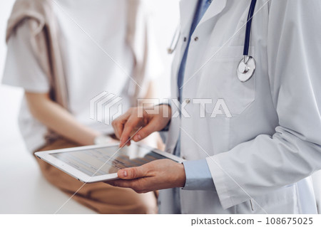 Doctor and patient in clinic. Friendly physician using tablet computer near a young woman. Medicine concept Doctor and patient in clinic. Friendly physician using tablet computer near a young woman. Medicine concept 108675025
