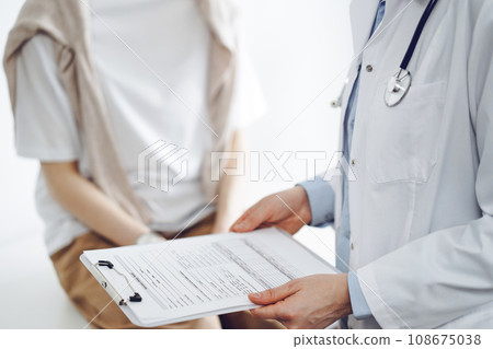Doctor and patient discussing perfect health exam results. Friendly physician keeping with hands clipboard with medical papers near young woman. Medicine concept 108675038