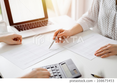 Accountant using a calculator and laptop computer for counting taxes with a client or a colleague at white desk in office. Teamwork in business audit and finance Accountant using a calculator and laptop computer for counting taxes with a client or a colleague at white desk in office. Teamwork in business audit and finance 108675453
