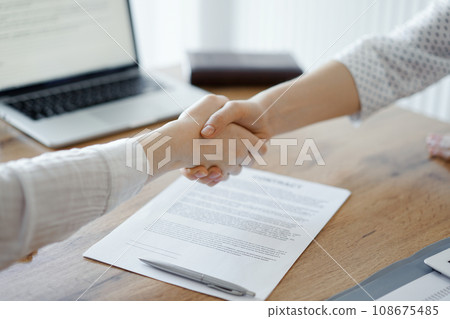 Business people shaking hands above contract papers just signed on the wooden table, close up. Lawyers at meeting. Teamwork, partnership, success concept Business people shaking hands above contract papers just signed on the wooden table, close up. Lawyers at meeting. Teamwork, partnership, success concept 108675485