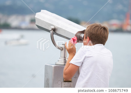 The boy looks at the observation deck in a tourist handheld telescope. The boy looks at the observation deck in a tourist handheld telescope. 108675749