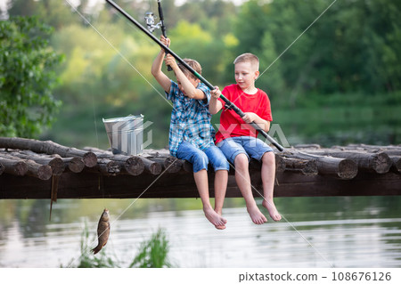 Happy friends boys caught a fish with a fishing rod. Children on a fishing trip. 108676126