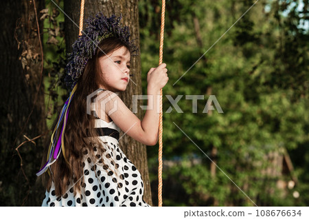 A small and beautiful girl in a dress is swinging on a swing. A small and beautiful girl in a dress is swinging on a swing. 108676634