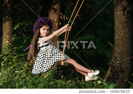 A small and beautiful girl in a dress is swinging on a swing. A small and beautiful girl in a dress is swinging on a swing. 108676635