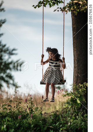 A small and beautiful girl in a dress is swinging on a swing. 108676636