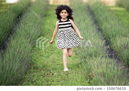 A little girl runs between lavender rows in a dress. A little girl runs between lavender rows in a dress. 108676638