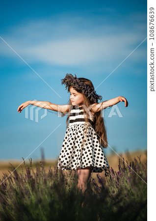 A small and beautiful girl walks in a park with a lavender field A small and beautiful girl walks in a park with a lavender field 108676639