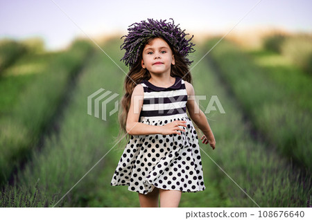 A little girl runs between lavender rows in a dress. 108676640