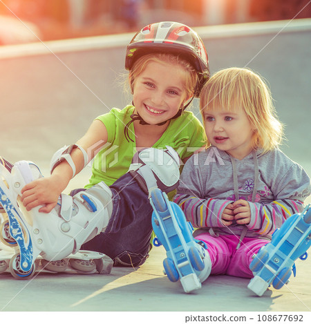 Cute little sisters in a roller skates sitting on the street 108677692