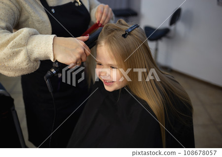 the hairdresser in the barbershop combing the hair of a little cute girl the hairdresser in the barbershop combing the hair of a little cute girl 108678057