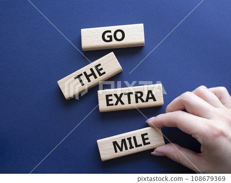 Go the extra mile symbol. Wooden blocks with words Go the extra mile. Businessman hand. Beautiful deep blue background. Business and Go the extra mile concept. Copy space. Go the extra mile symbol. Wooden blocks with words Go the extra mile. Businessman hand. Beautiful deep blue background. Business and Go the extra mile concept. Copy space. 108679369