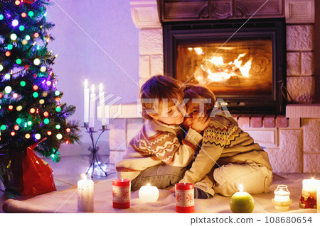 Cute toddler boys, blond twins playing together and lookinig on fire in chimney. Family celebrating xmas holiday 108680654