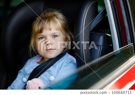 Sad upset little kid girl sitting in car in traffic jam during going for summer vacation with his parents. Tired, exhausted child not happy about long journey. Crying baby. 108680715