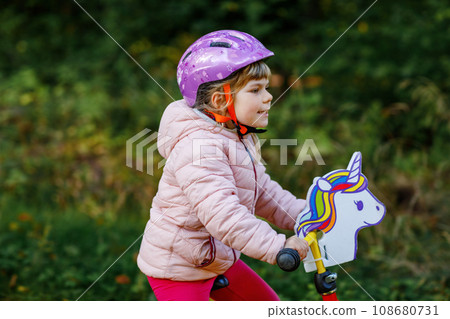 Child riding balance bike. Kids on bicycle in sunny forest. Little girl enjoying to ride glider bike on warm day. Preschooler learning to balance on run bicycle in safe helmet. Sport activity 108680731